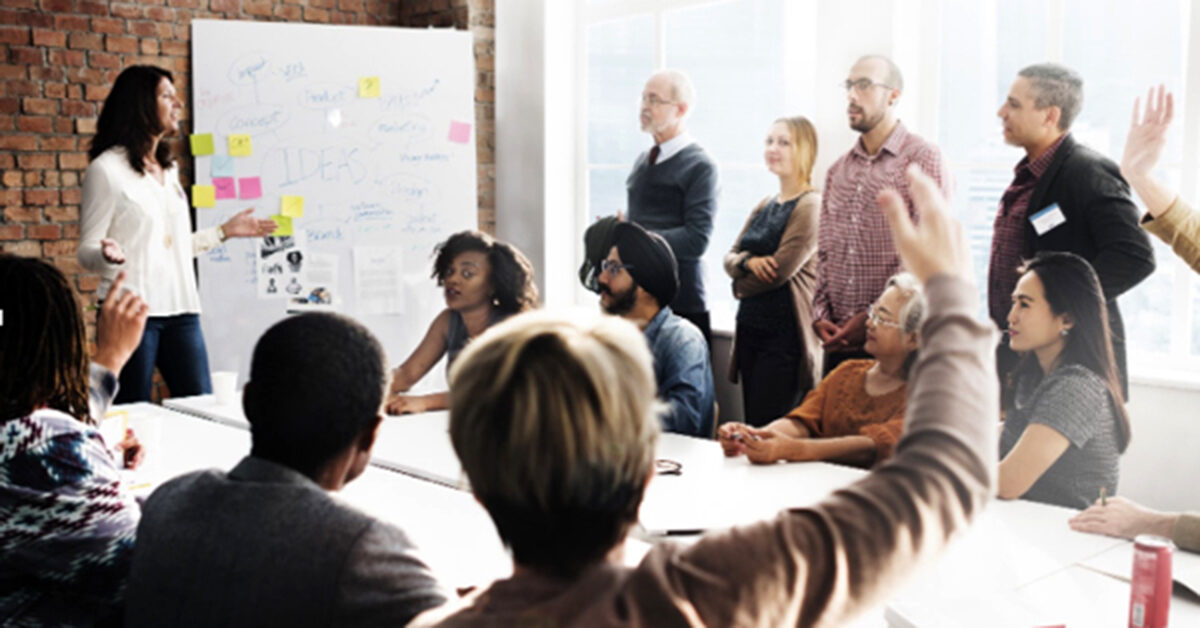 A meeting of professionals with someone raising their hand to speak