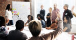 A meeting of professionals with someone raising their hand to speak
