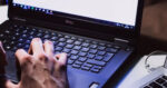 A person's hand is rested on a Dell computer next to a Mac computer