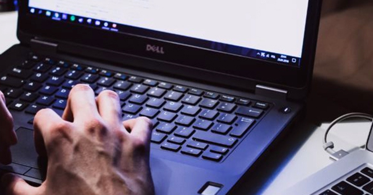 A person's hand is rested on a Dell computer next to a Mac computer