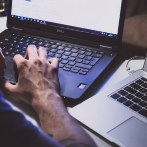 A person's hand is rested on a Dell computer next to a Mac computer