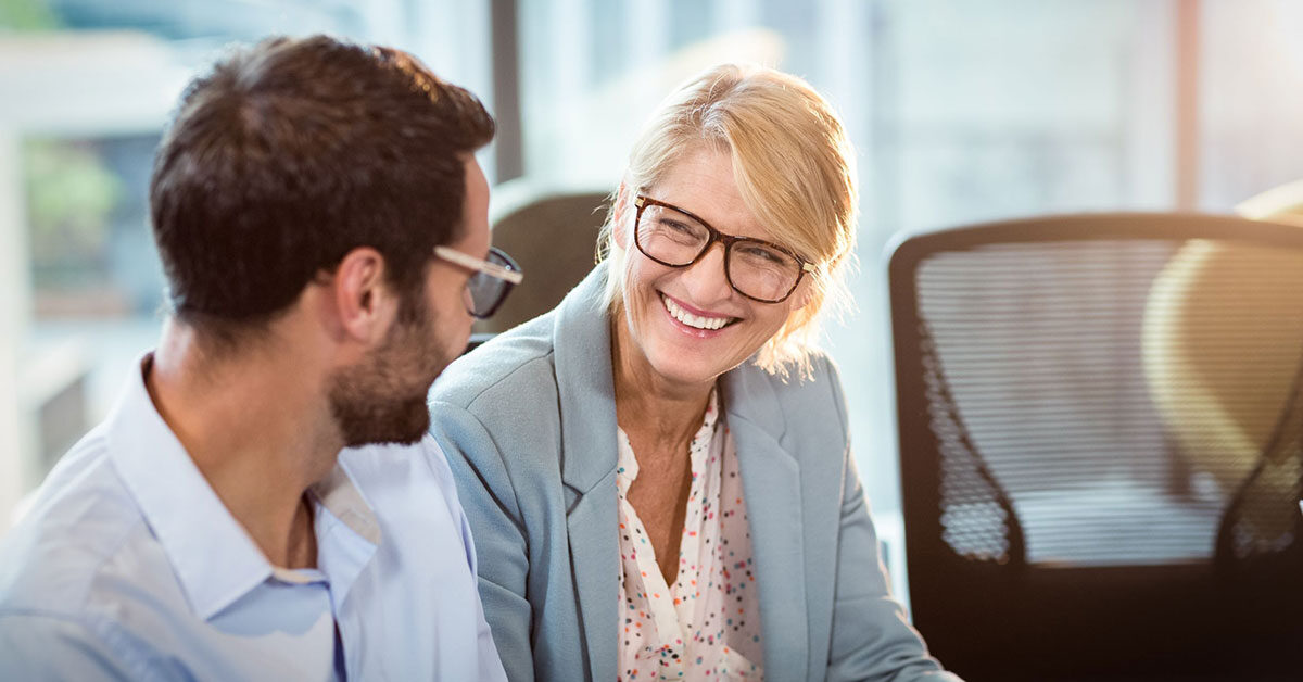 Smiling woman sitting with colleague using educational leadership skills in the workplace