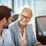 Smiling woman sitting with colleague using educational leadership skills in the workplace