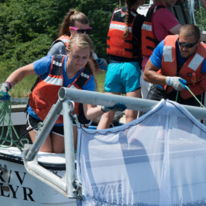 UNE students on a boat putting a net into the water to investigate food systems sustainability