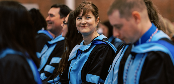 A smiling woman in a graduation gown poses for the camera, celebrating her academic achievement.