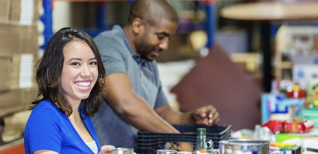 Young woman volunteering in food bank warehouse, sorting donations