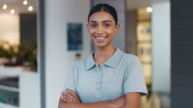 Portrait, woman and confidence as physiotherapist in gym, rehabilitation clinic or wellness practice. Female person, pride and arms crossed with smile, personal trainer or coach for physio exercise