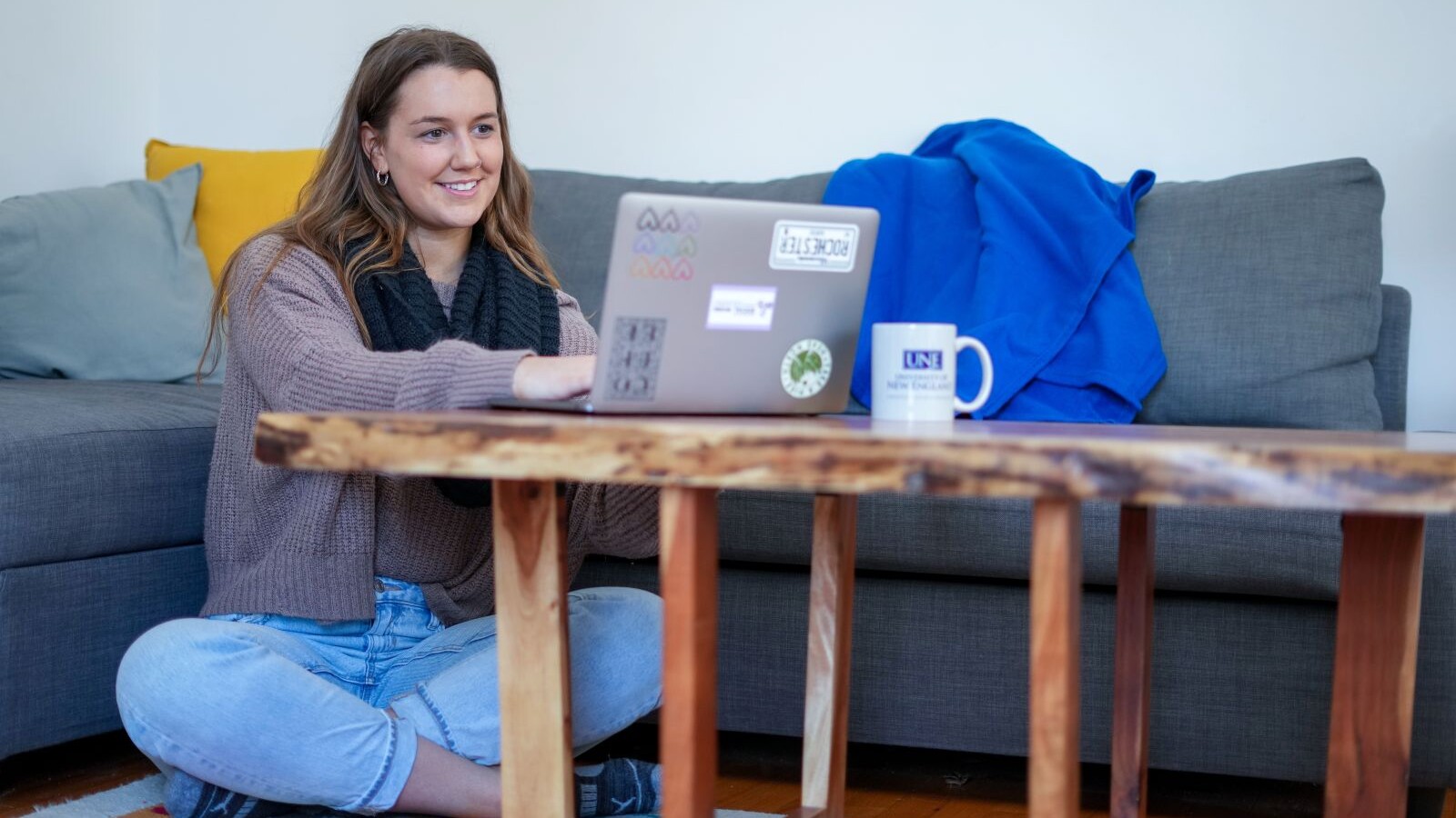 Woman sitting on the floor against a couch working on her laptop