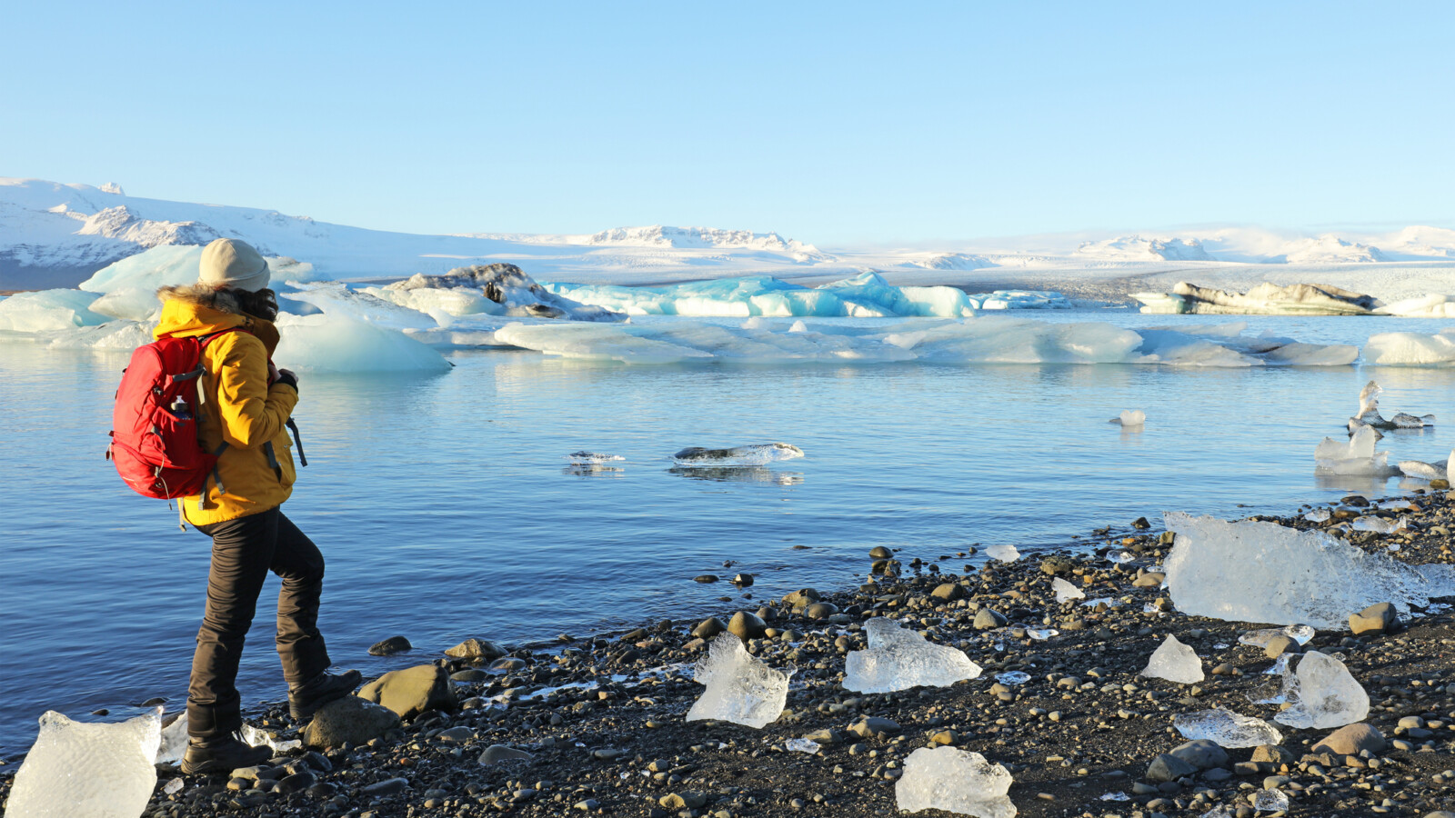 Female traveller is standing at the edge of Jokulsarlon glacial lagoon in Iceland on a beautiful sunny winter day.
