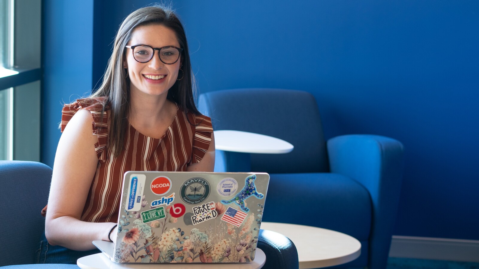 Smiling student sitting in a blue chair using a laptop in a blue-painted room