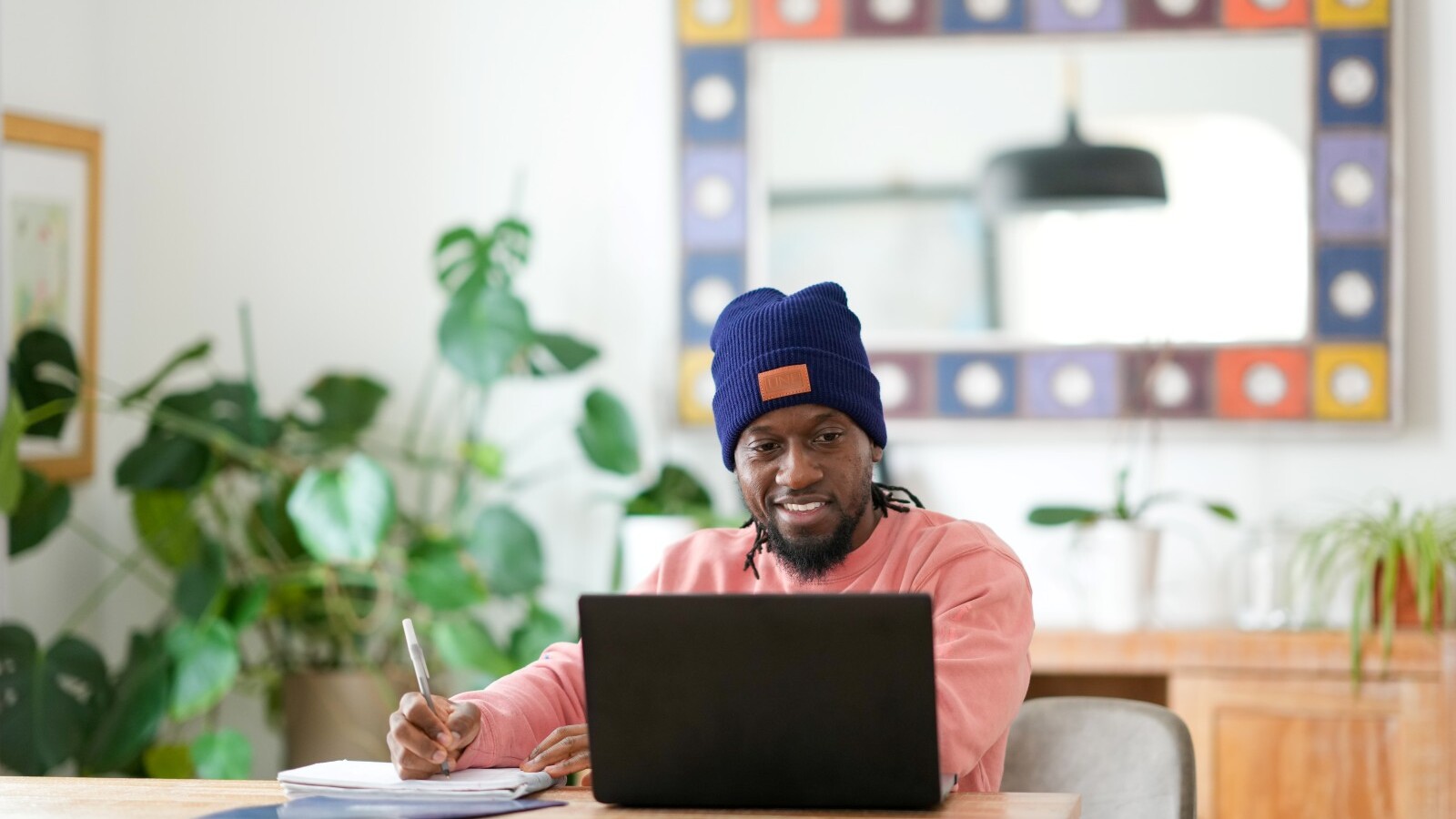 Student sitting at a table with a laptop and writing in a notebook