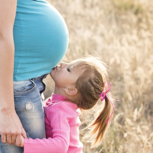 Young child kissing the belly of a pregnant woman