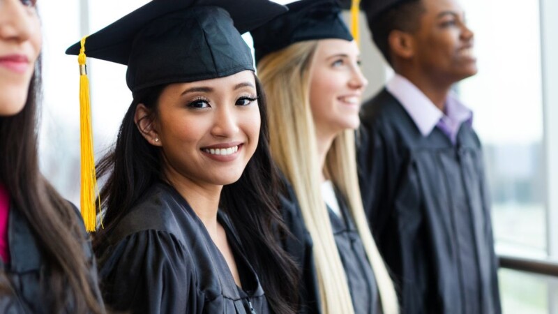 Diverse group of young adults proudly wearing graduation gowns and caps.