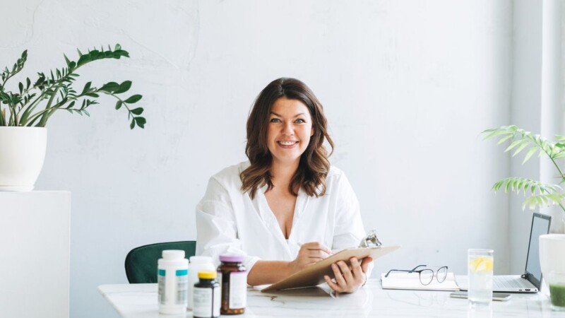 Young smiling brunette woman doctor nutritionist plus size in white shirt working at laptop at modern bright office room. The doctor prescribes prescription for medicines and vitamins at clinic