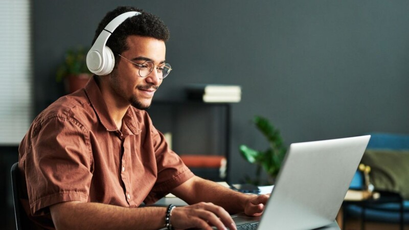Young smiling man in headphones typing on laptop keyboard