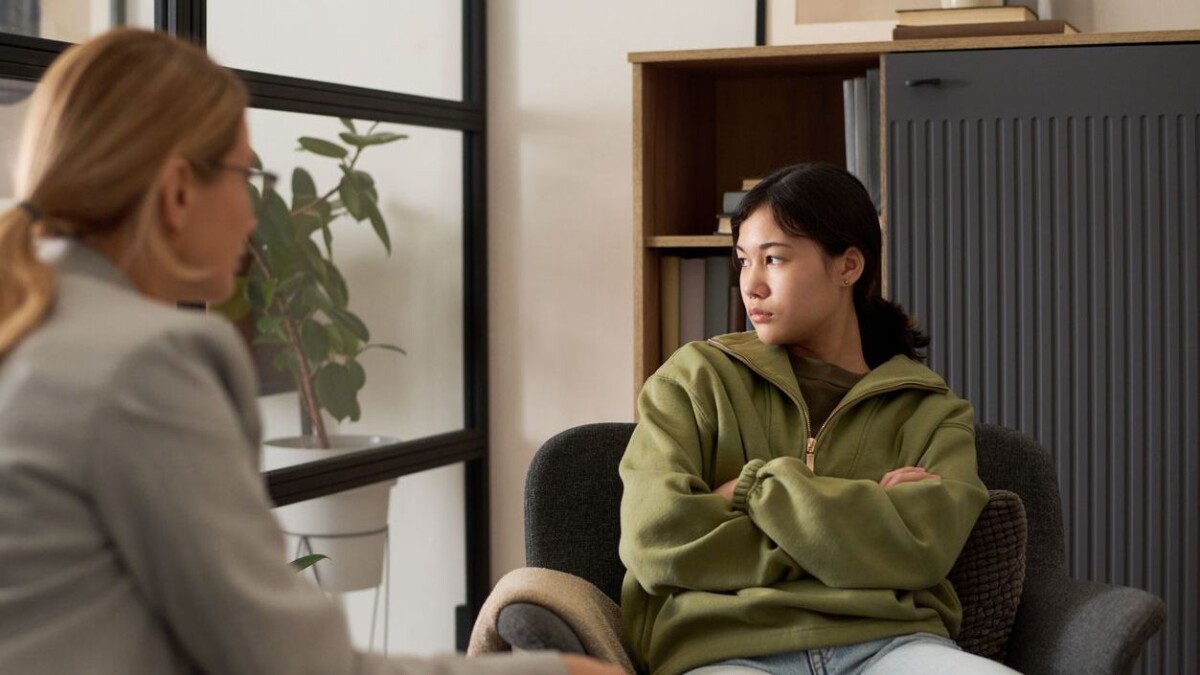 Portrait of angry teenage girl stonewalling therapist during counseling meeting