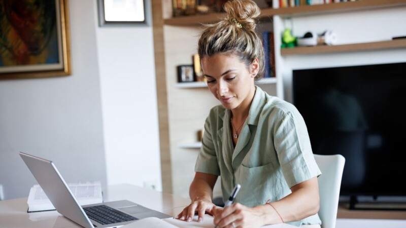 Beautiful young woman taking notes while learning from home