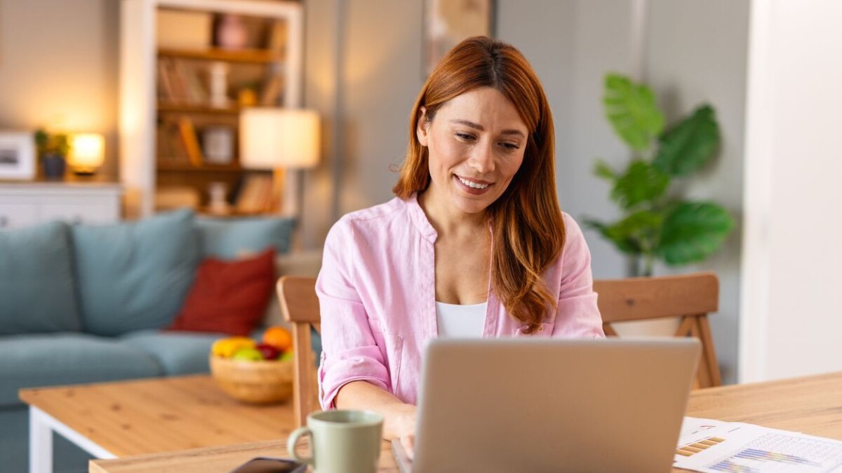 Woman smiling while working on a laptop with a coffee mug nearby