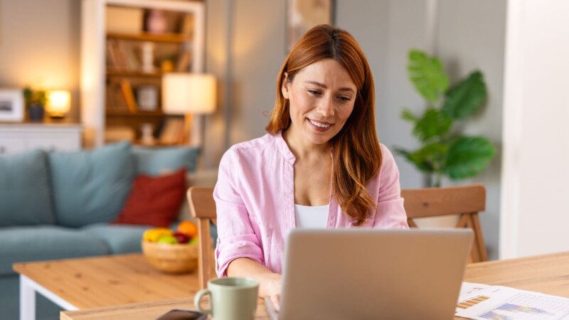 Woman smiling while working on a laptop with a coffee mug nearby