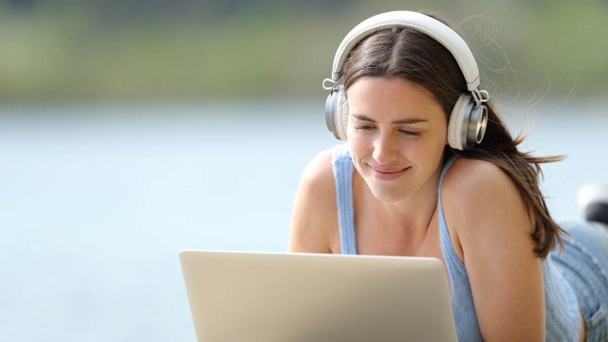 Woman with headphones using laptop lying on pier