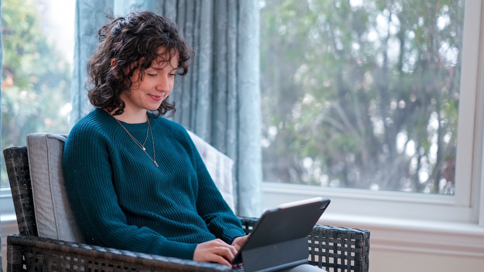 Smiling student sitting in a chair by windows working on a laptop