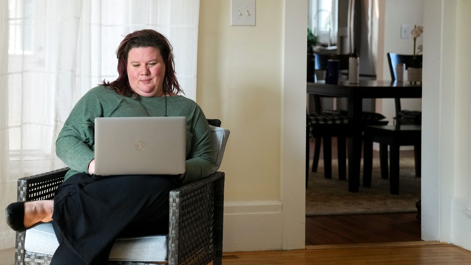 Adult student sitting in a chair with a laptop next to a side table with a plant and a mug